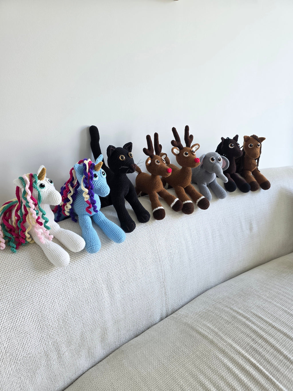 Collection of handmade amigurumi crochet animals including horses, cats, reindeer, unicorns and an elephant.