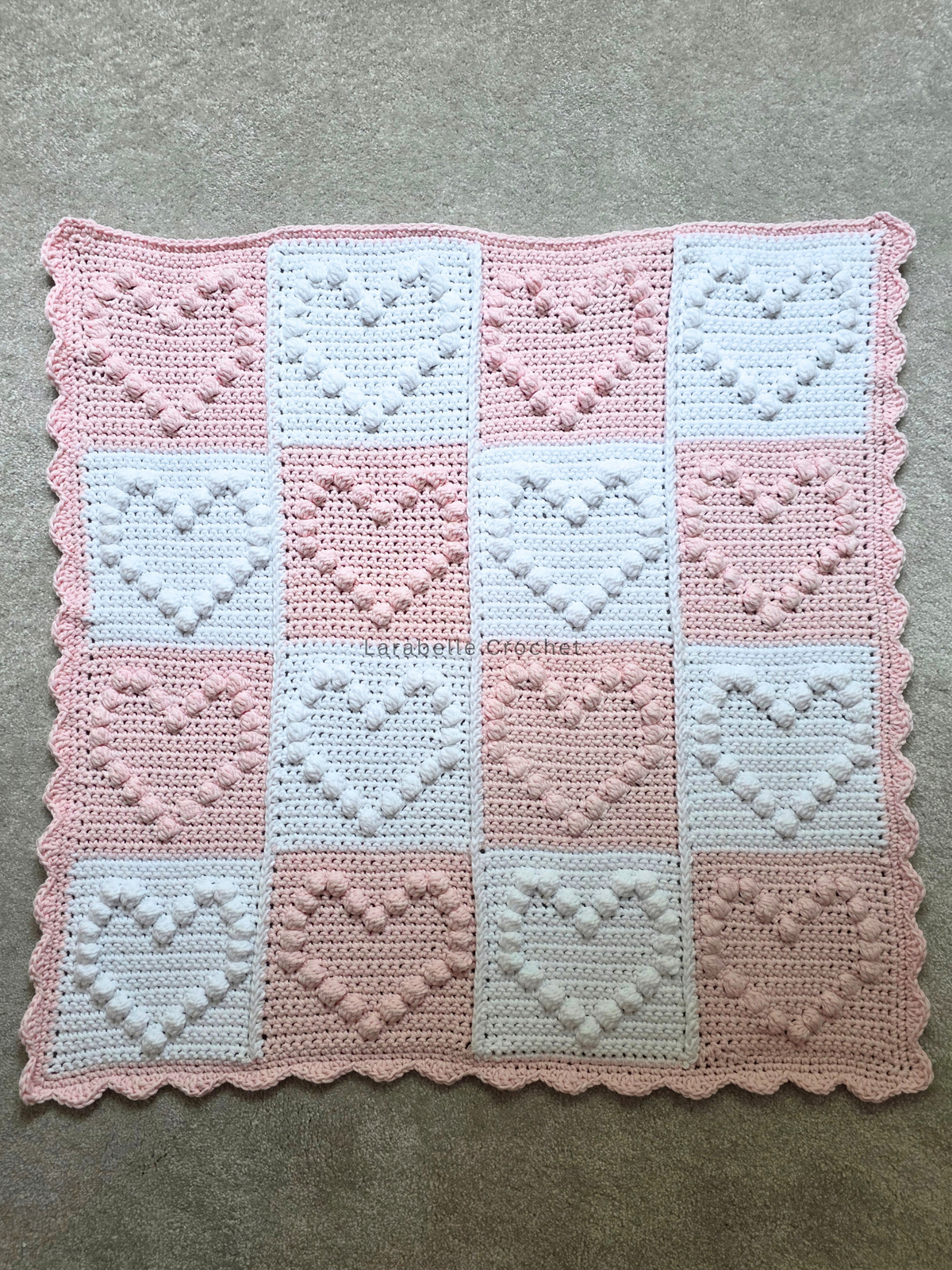 Full view of crochet baby blanket featuring small hearts in a patchwork grid of 4 x 4.
