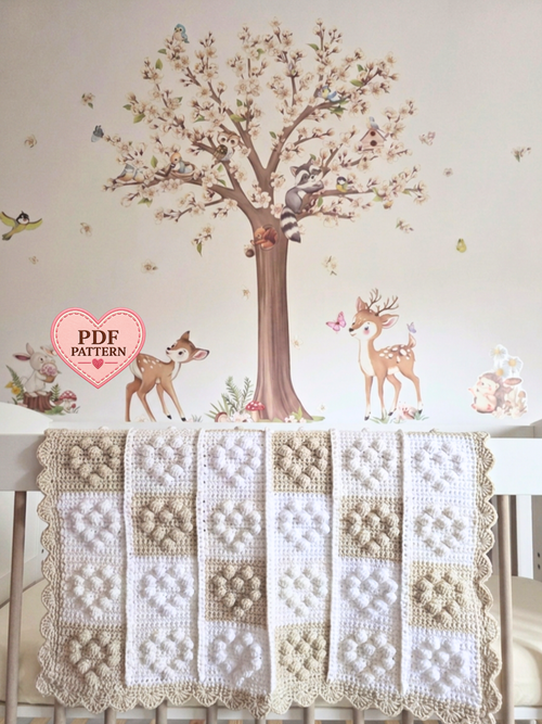A handmade crochet baby blanket with a patchwork design of cream, beige, and white squares with small hearts.