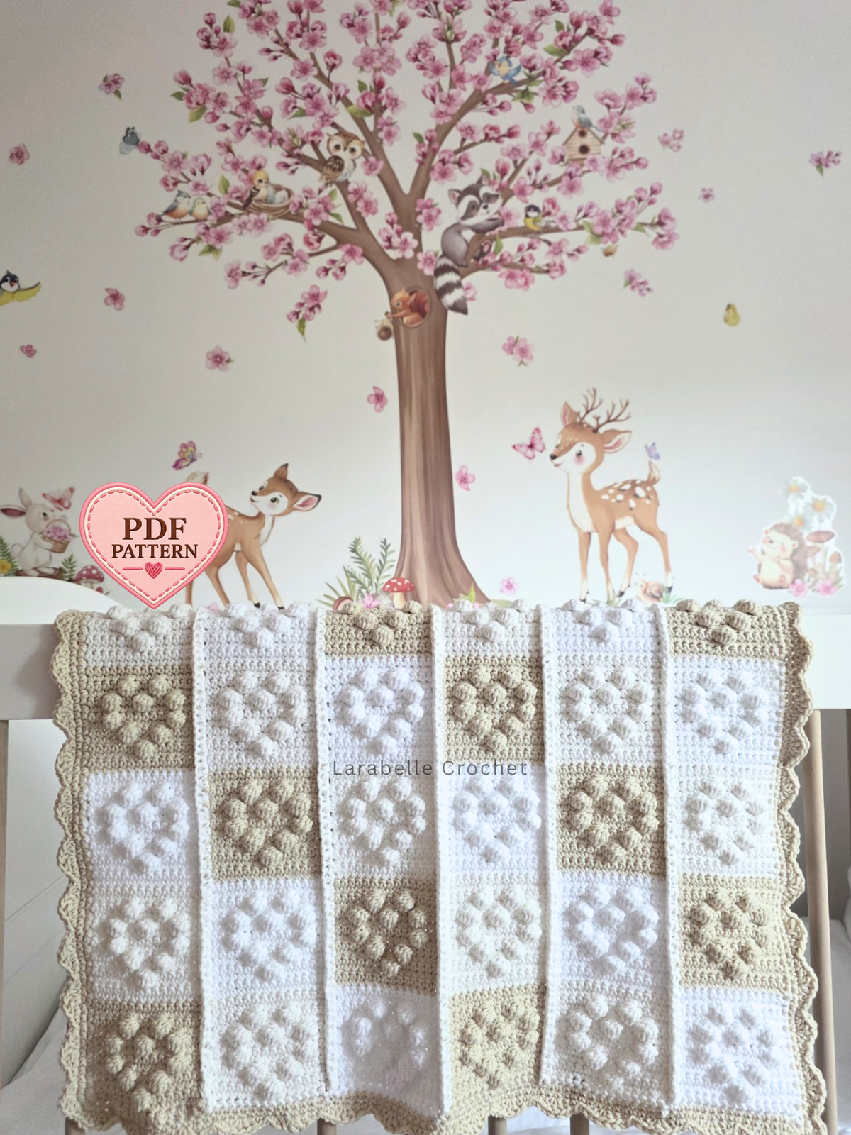 A handmade crochet baby blanket with a patchwork design of cream, beige, and white squares with small hearts.