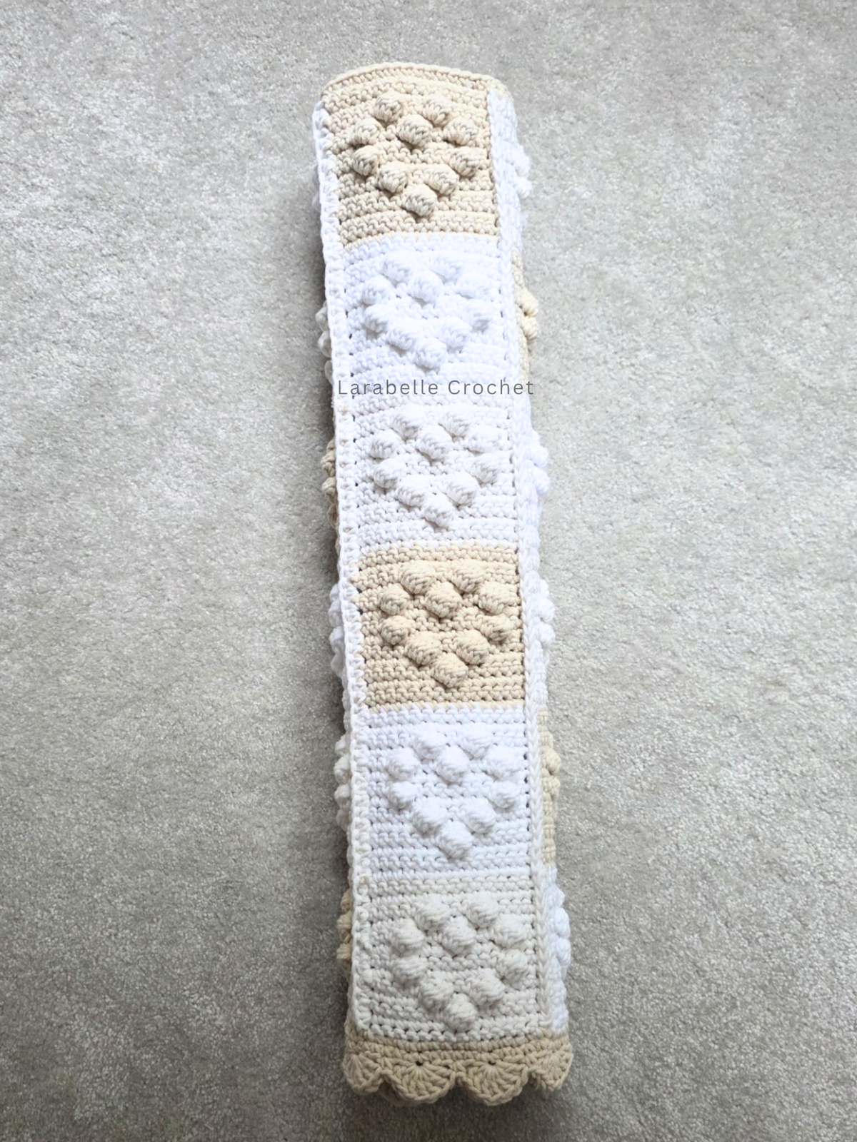 Rolled up crochet baby blanket featuring small hearts in a patchwork grid of 6 x 6.